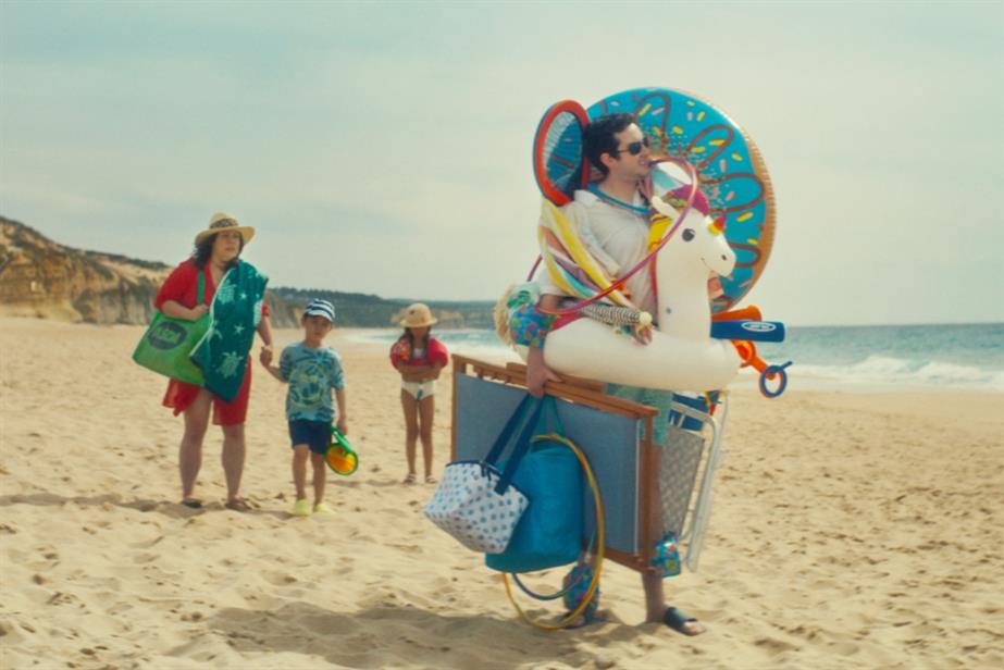 A man stands in front of his family with many beach props. He is surveying the area and they are looking at him in distress.