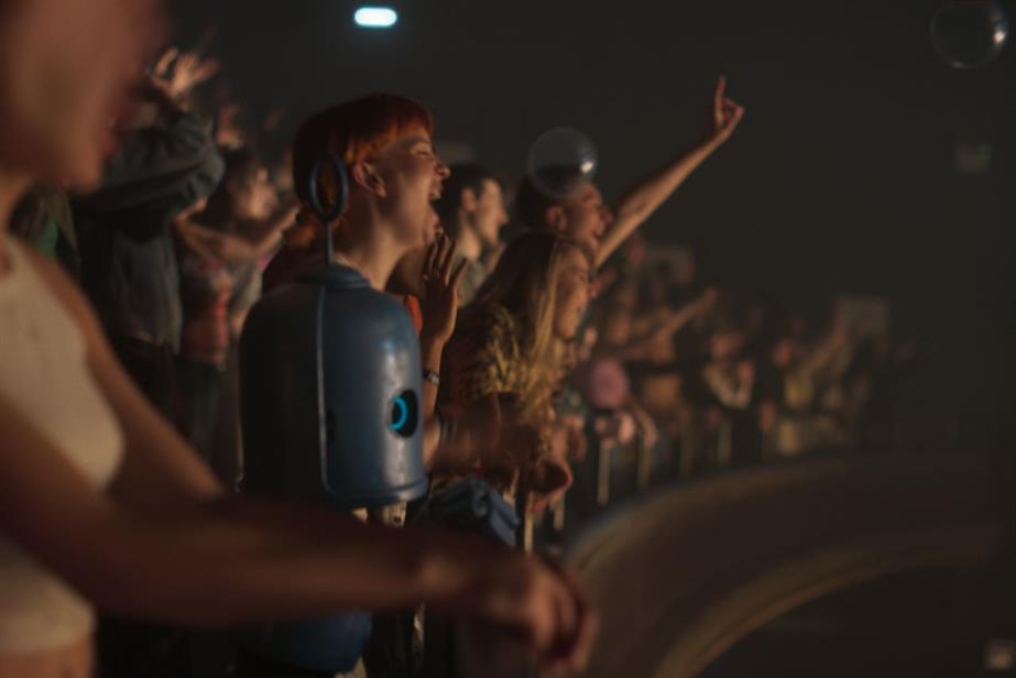 A still from the ad showing robot mascot Bubl in a crowd at a gig