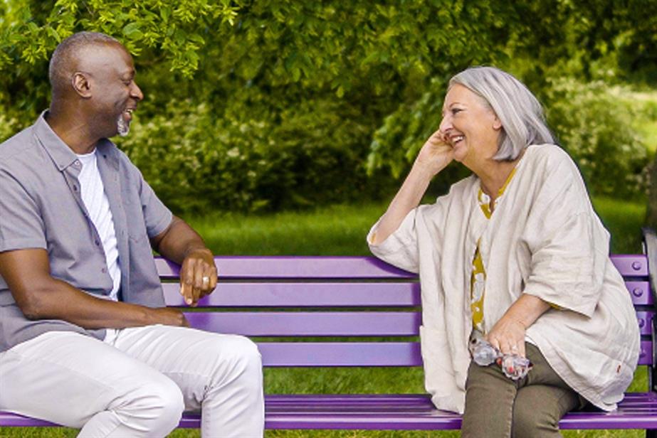 Two people sit on a bench, talking to each other and laughing