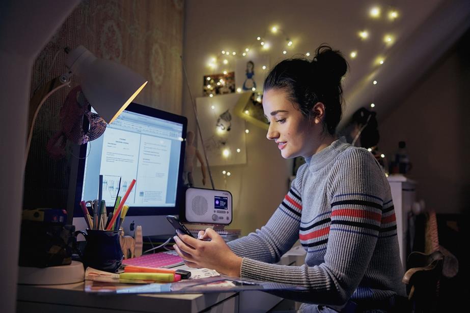 A young woman listens to the radio in front of her computer.